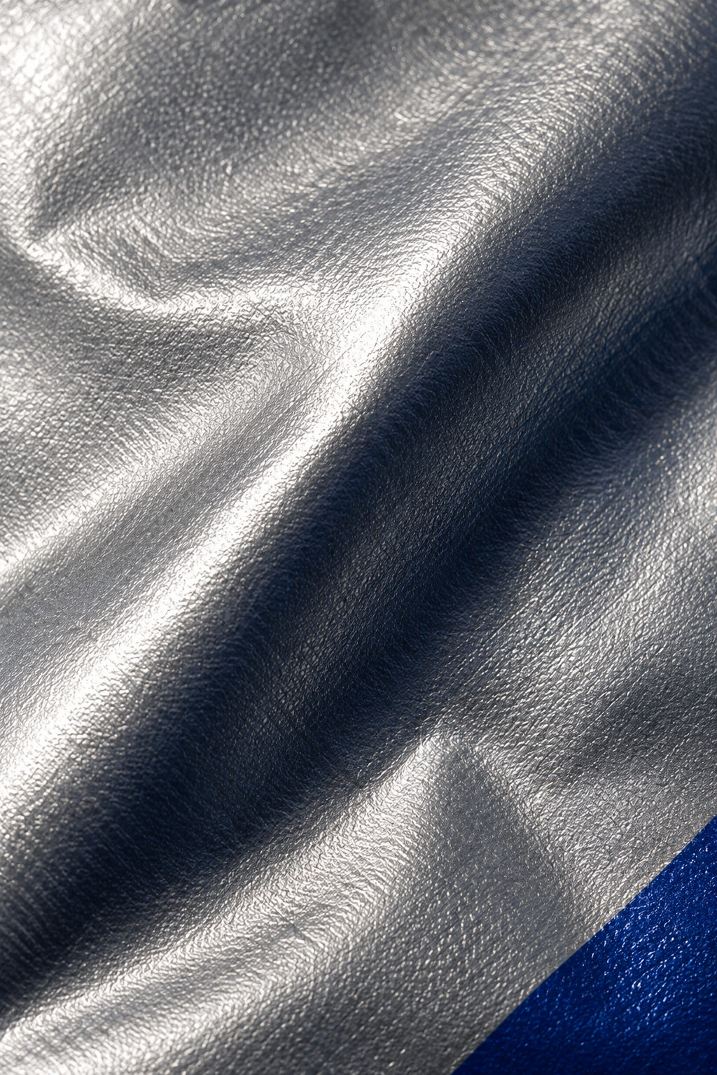 Extreme close-up of silver film texture, a sculptural fold and a small cobalt edge