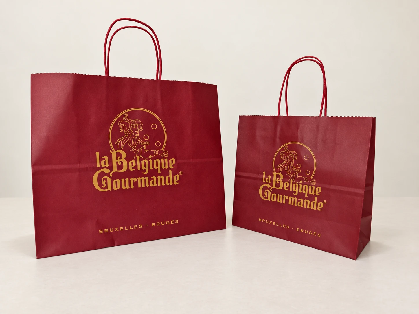 Two red paper carriers with gold print and rope handles