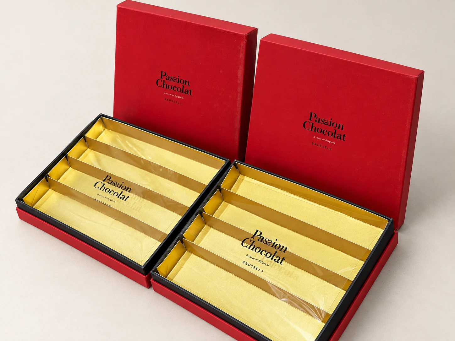 Two red rigid chocolate boxes with lids, open to show gold compartment inserts