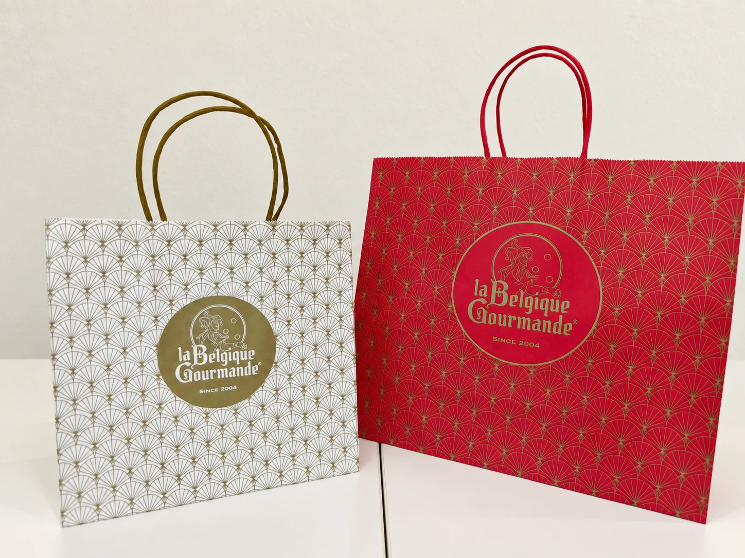 Two paper carriers, white and red, with a fan pattern, gold print and rope handles