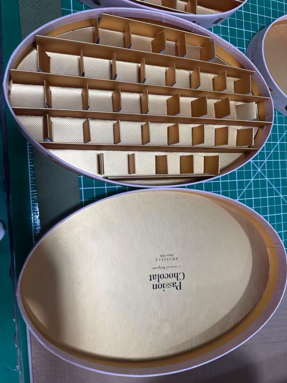 Open oval confectionery box showing the compartment layout and separate lid.